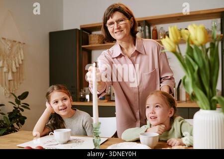 Senior Woman Lighting Candle While Sitting with Two Children Stock Photo