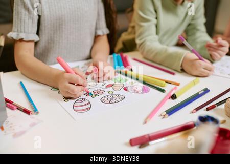 Girls Drawing Easter Eggs with Colored Markers at Table Indoors Stock Photo