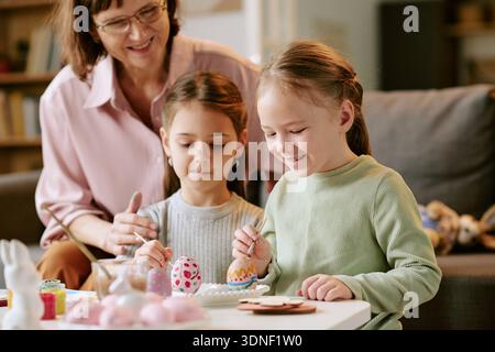 Two Girls Painting Easter Eggs While Smiling with Middle Aged Woman Stock Photo