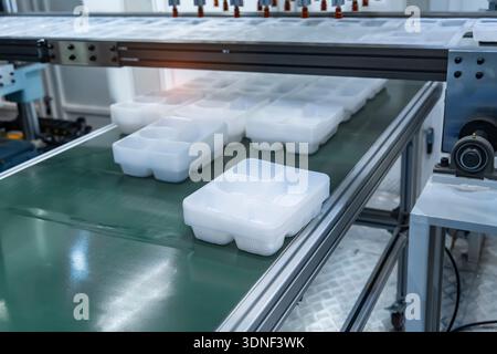 Stack of polypropylene food containers on conveyor belt of automatic plastic injection molding machine,automated technology concept Stock Photo