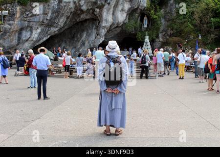 Catholic monk praying the rosary in front of the Grotto of Massabielle while pilgrims gather nearby, Lourdes, France, taken in July 2024. Stock Photo