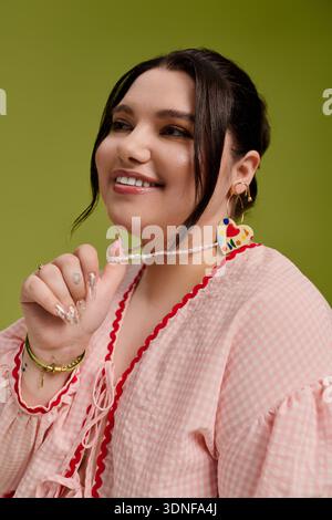 Beautiful plus size woman smiles warmly while holding a playful necklace, radiating joy. Stock Photo