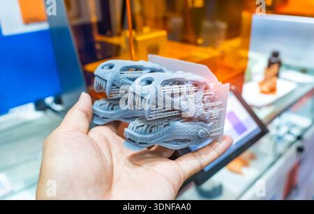 hand holding 3D printer printing dragon head figure close-up. Stock Photo