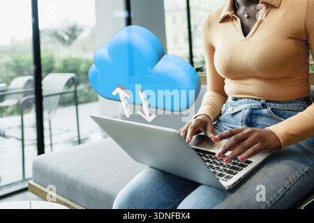 Person using laptop with cloud upload symbol in modern setting near window in the afternoon Stock Photo