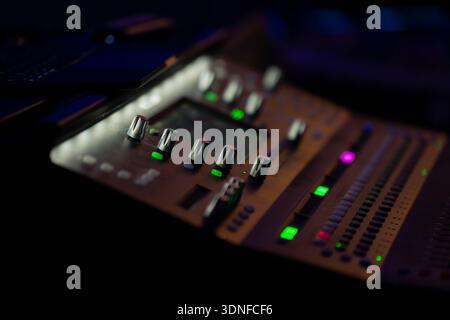 Stage audio control desk detail showing mixer knobs and LED status lights on dark console, selective focus for live sound engineering concept Stock Photo