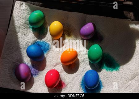 Top view of multiple dyed easter eggs in bright blue, green, yellow, orange, red, and purple drying on a textured paper towel Stock Photo