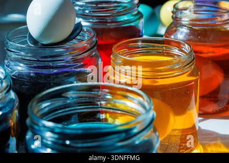 Close up of a hand using a spoon to dip a white egg into a glass jar with colorful easter dye Stock Photo