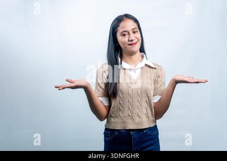 A happy Indonesian woman holding her hands out to the sides, presenting two choices or balancing options on a clean white background. Stock Photo