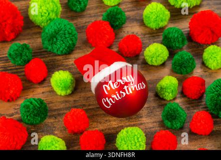 Red Christmas ball with words Merry Christmas on wooden background with pompoms Stock Photo