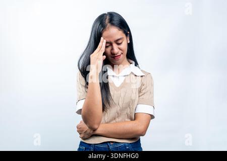 Young Southeast Asian woman looking down while touching her forehead with a stressed and worried expression on a white background. Stock Photo