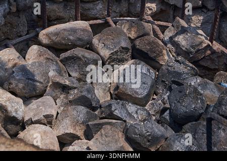Rough dark stones filling a metal gabion cage, creating a textured background Stock Photo