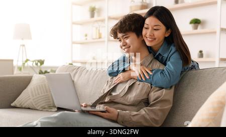 Couple Enjoys Time Together While Using a Laptop in a Cozy Living Room During Daytime Stock Photo