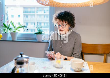 Middle Aged Woman Checking Smartphone During Breakfast At Home Morning Digital Connection Lifestyle Stock Photo