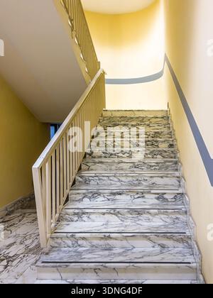 White marble stairs with metal railing and yellow walls with gray stripes, internal staircase of a public hospital building Stock Photo