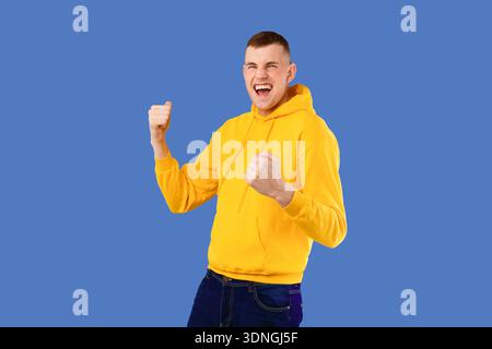 Overjoyed caucasian man shouting and shaking fists, celebrating big success over blue studio background, free space Stock Photo