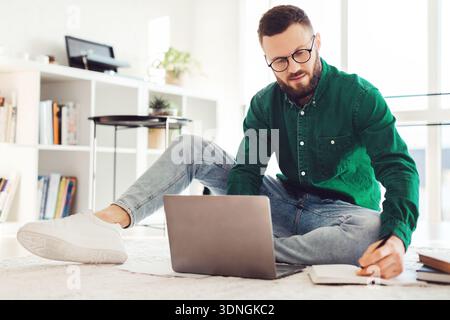 Man Taking Notes Using Laptop Sitting On Floor At Home Stock Photo