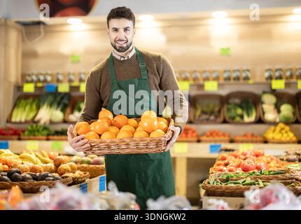 Male employees in uniform carries a wicker basket with oranges in grocery shop Stock Photo