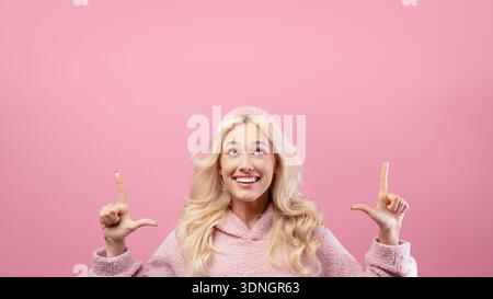 Woman Shows Hand Signs Against Pink Background With Cheerful Expression During Indoor Activity Stock Photo