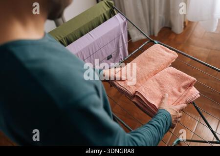 View from shoulder of unrecognizable person folding clean, soft pink towels on laundry drying rack, performing daily household chores and maintaining Stock Photo