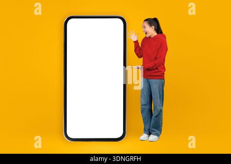 Young Woman Shows Phone and Smiles With Bright Yellow Background in Indoor Space Stock Photo