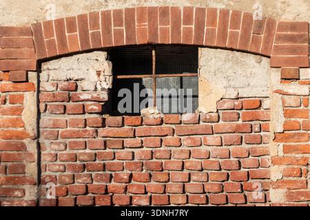 Weathered brick window with arched lintel and iron crossbar, revealing layered textures and timeworn materials, perfect for architectural storytelling Stock Photo