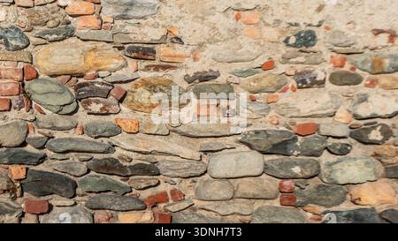 Irregular stones and scattered bricks set in aged mortar create a tactile, timeworn surface, perfect for rustic backgrounds, architectural textures, a Stock Photo