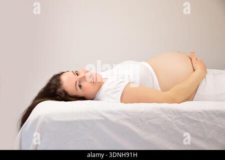 Pregnant woman lying down on a bed at home Stock Photo