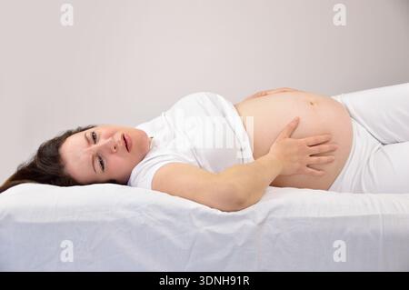 Pregnant woman holding her stomach in pain on the bed Stock Photo