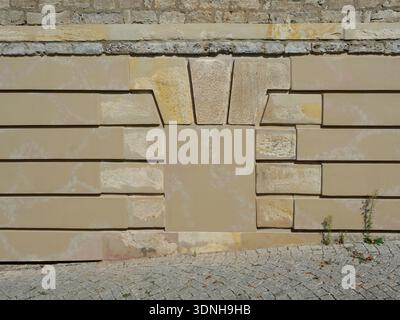 Rough stone wall with light brown blocks, bricked-up opening, and paved walkway. Signs of age and weathering visible. Copyspace. Stock Photo