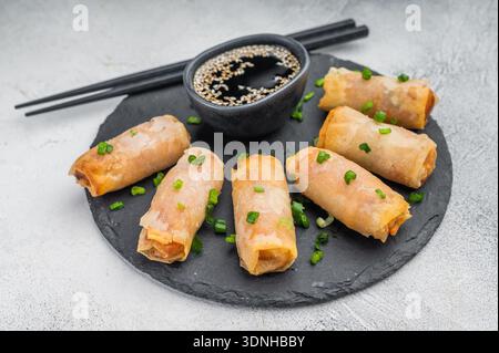 Crispy Egg rolls arranged on round slate plate with soy sauce and sesame seeds flat lay light background. Stock Photo