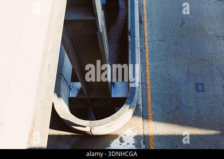 Concrete meets asphalt as a curved structure stands above a road. Shadows create patterns on the pavement in bright daylight. The scene shows urban de Stock Photo