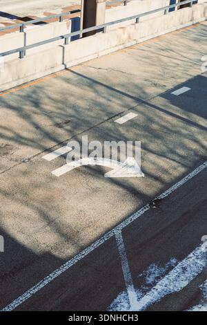 A road surface shows a left turn arrow marking. The sunlight creates shadows on the asphalt. The area appears empty with no vehicles present. Stock Photo