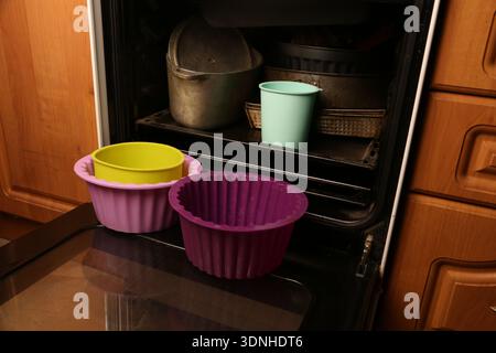 Several silicone baking molds in different colors sit on a shelf inside a kitchen oven. Some metal containers are also visible in the background. The Stock Photo