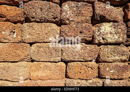 Laterite rock wall texture with porous reddish blocks. Natural stone background for architecture, heritage, and tropical landscape design. Stock Photo