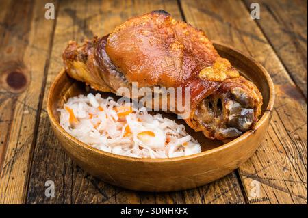 Crispy roasted pork knuckle shank with golden crackling rind served with fermented cabbage slaw on rustic wooden background. Stock Photo