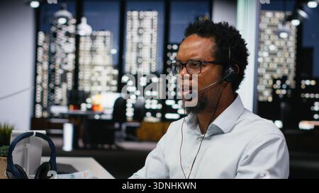 Startup helpdesk system administrator in office speaking in headset microphone, responding to service alerts. IT professional doing tech support, helping users across remote infrastructure Stock Photo