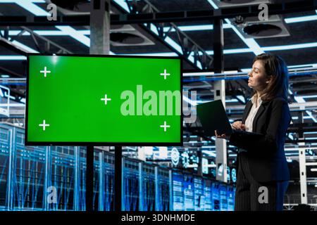 Isolated screen monitor used by server room employee doing maintenance with laptop, AR visualization graphics. Woman monitoring data center rigs with chroma key display, holographic VFX compositing Stock Photo