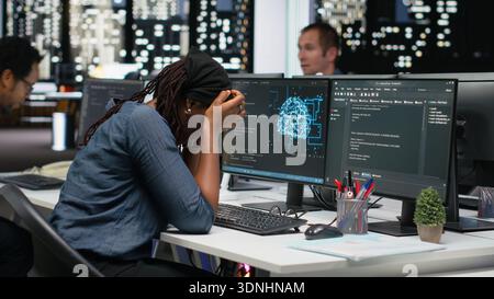 Sleepy IT specialist in office typing code on computer, developing machine learning model late at night. Tired system administrator writes programming language scripts, working overtime Stock Photo
