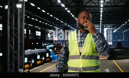 Warehouse technician uses radio communication to guide machinery operation, managing engineering responsibilities for industrial environment. Manpower for manufacturing process. Stock Photo