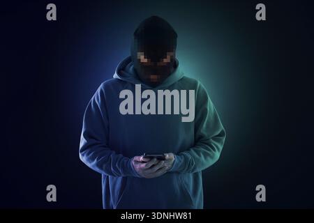 Criminal in mask holding phone against dark background. Man's face party pixelated Stock Photo
