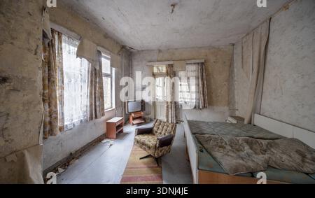 Abandoned hotel room with bed, armchair and television in a dilapidated hotel, Lost Place, Saxony-Anhalt, Germany Stock Photo