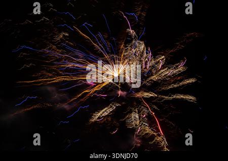 Vibrant fireworks explosion at night: Long exposure captures colorful bursts and radiating trails against deep black sky, no stars visible. Stock Photo
