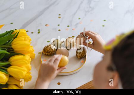 Smiling child wearing bunny ears with natural Easter eggs at home kitchen Stock Photo