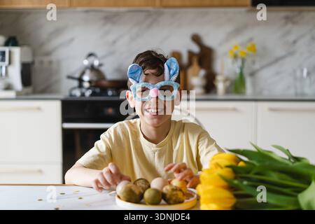 Smiling child wearing bunny ears with natural Easter eggs at home kitchen Stock Photo