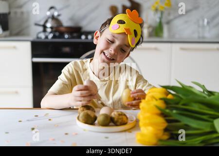 Smiling child wearing bunny ears with natural Easter eggs at home kitchen Stock Photo