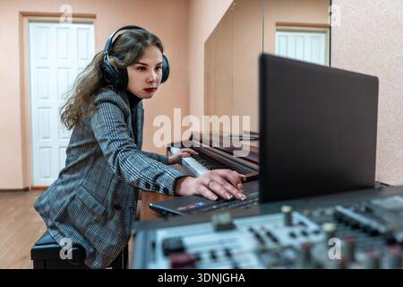 A professional female sound engineer at work, focused on operating a laptop and mixing console for audio recording or production. Stock Photo