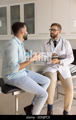 Focused doctor listening to male patient complaints taking paper notes Stock Photo