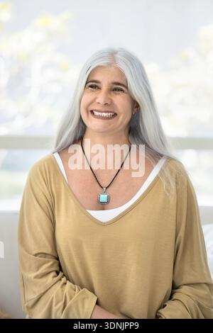 Vertical portrait of overjoyed middle-aged woman posing seated on couch Stock Photo