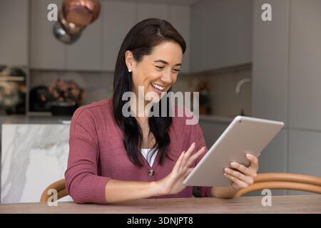 Woman using tablet while sitting at table in modern kitchen Stock Photo