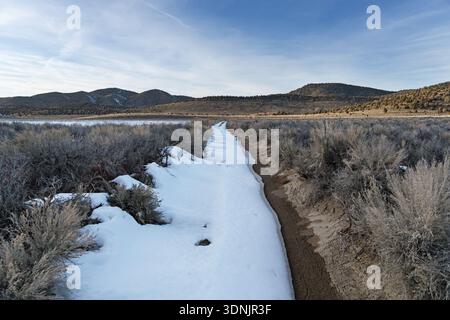 snow drift partially covers dirt doubletrack road in the Inyo Mountains of California Stock Photo